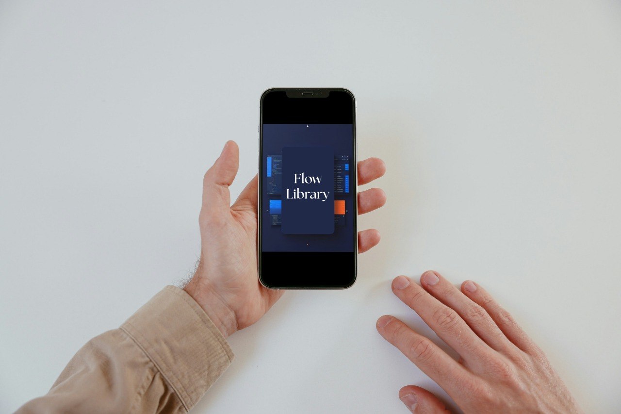 A person holds a black smartphone showing the Flow Library app on the screen against a plain white background.
